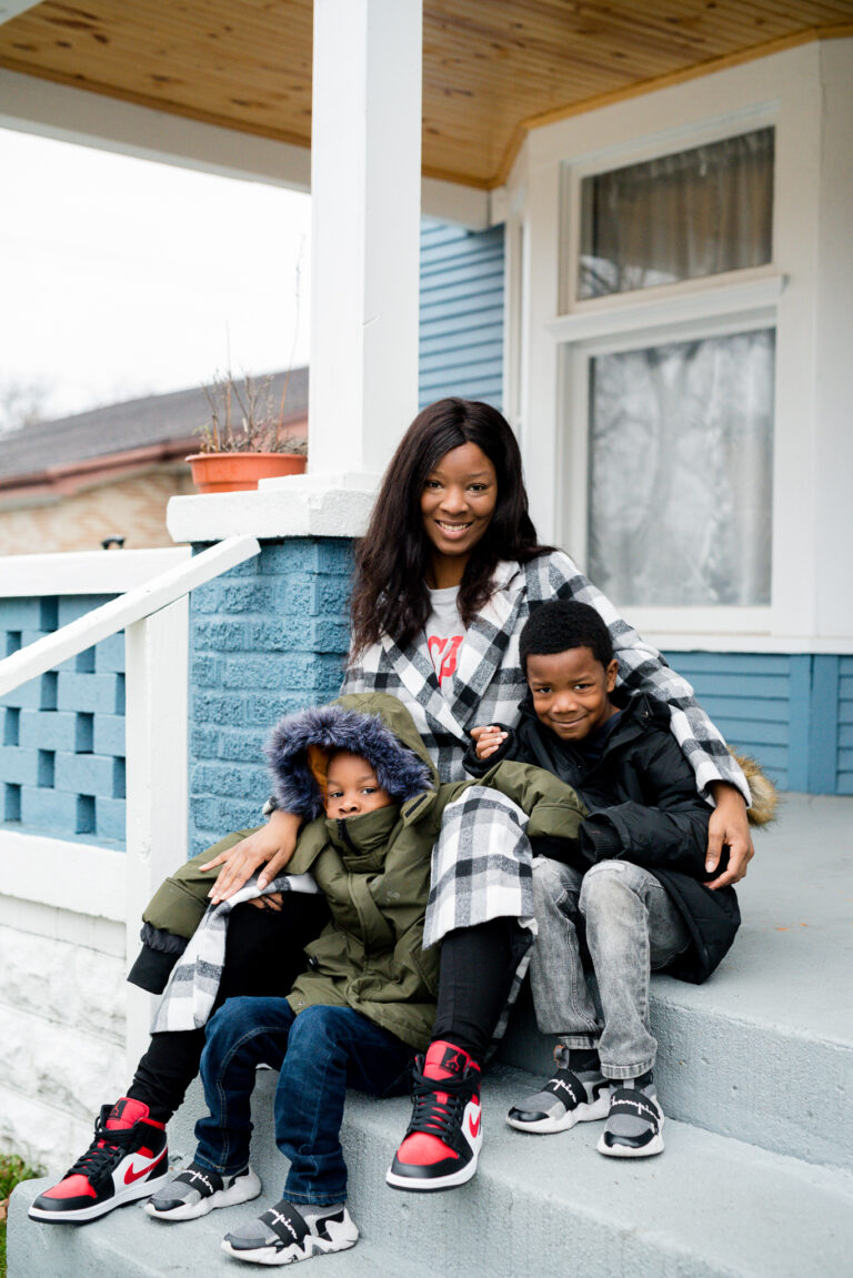 Photo of Dominique Baker seated with her two sons outside their home